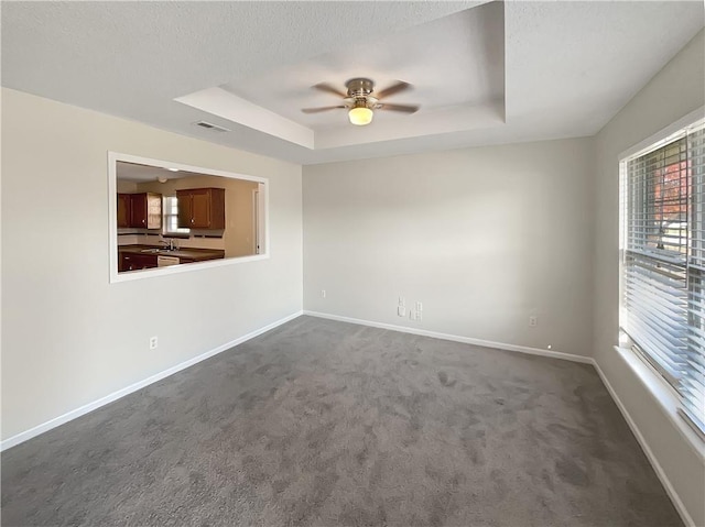 carpeted spare room with ceiling fan, sink, and a tray ceiling