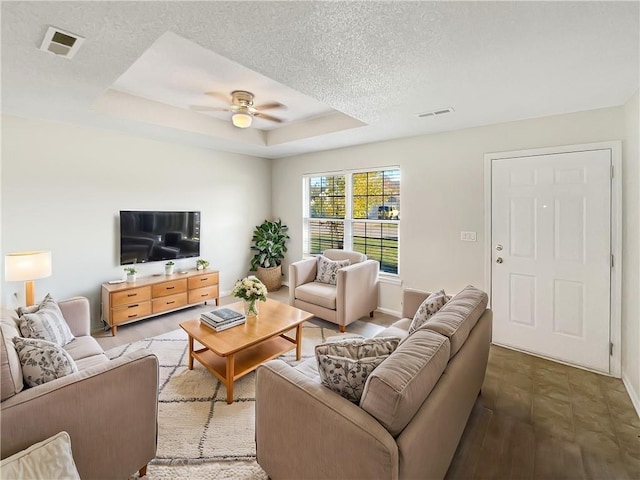 living room featuring a textured ceiling, wood-type flooring, ceiling fan, and a raised ceiling