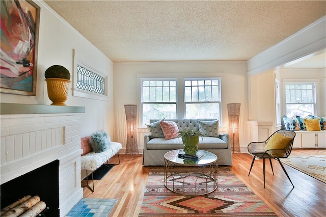 sitting room with a brick fireplace, plenty of natural light, light hardwood / wood-style flooring, and a textured ceiling