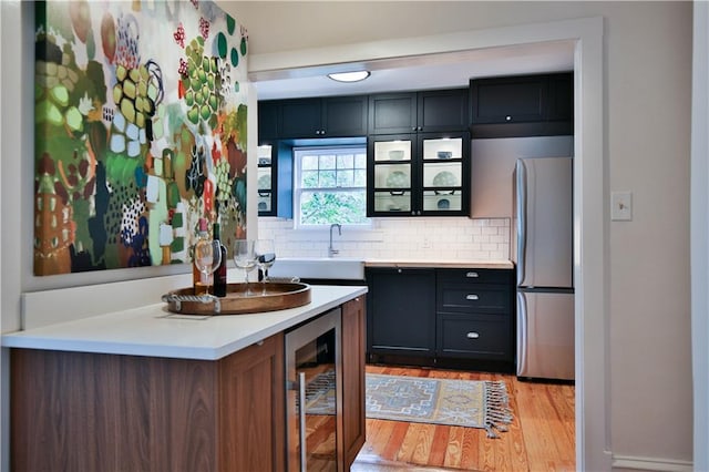 kitchen featuring beverage cooler, sink, tasteful backsplash, light hardwood / wood-style flooring, and stainless steel fridge