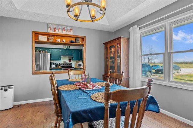 dining area with a textured ceiling, light hardwood / wood-style floors, and a notable chandelier