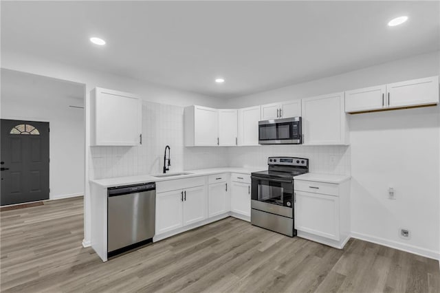 kitchen featuring appliances with stainless steel finishes, decorative backsplash, sink, light hardwood / wood-style floors, and white cabinets