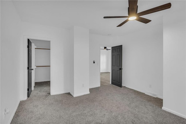 unfurnished bedroom with a closet, a spacious closet, light colored carpet, and ceiling fan