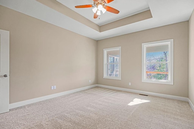 carpeted spare room with a tray ceiling, a healthy amount of sunlight, baseboards, and visible vents