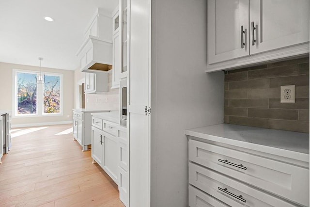 interior space featuring decorative backsplash, light countertops, light wood-style flooring, and decorative light fixtures