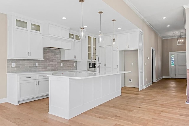 kitchen featuring a center island with sink, a sink, tasteful backsplash, white cabinetry, and light wood finished floors