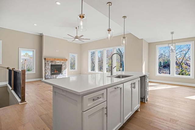 kitchen featuring an island with sink, a sink, light wood-style floors, a stone fireplace, and light countertops