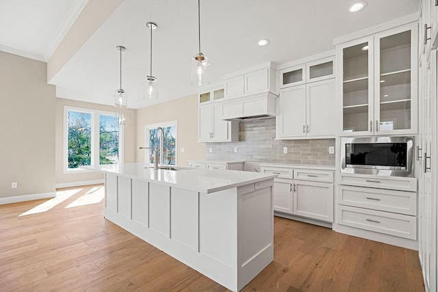 kitchen featuring stainless steel microwave, decorative backsplash, light wood-style flooring, white cabinetry, and a sink