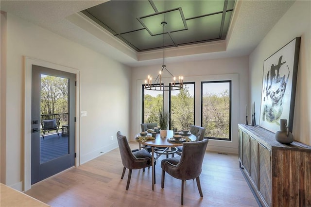 dining room with light hardwood / wood-style flooring, a raised ceiling, and a notable chandelier