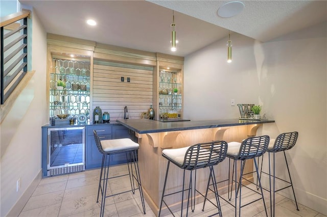 bar with pendant lighting, a textured ceiling, wine cooler, and wooden walls