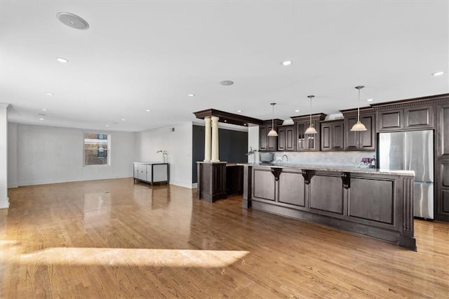 kitchen featuring pendant lighting, stainless steel fridge, light hardwood / wood-style floors, a kitchen bar, and dark brown cabinetry