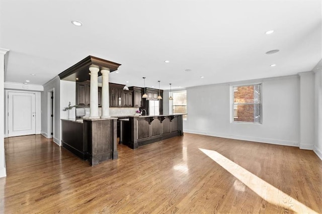 kitchen with hanging light fixtures, crown molding, wood-type flooring, dark brown cabinets, and a kitchen island