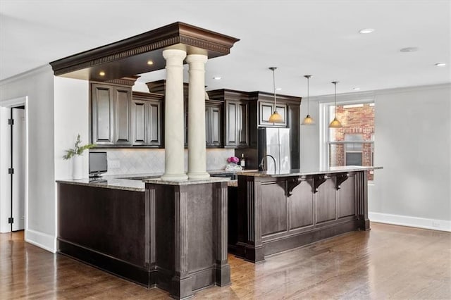 kitchen with a kitchen bar, stainless steel fridge, decorative columns, and decorative light fixtures