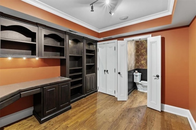 office area with light wood-type flooring, rail lighting, a raised ceiling, crown molding, and built in desk