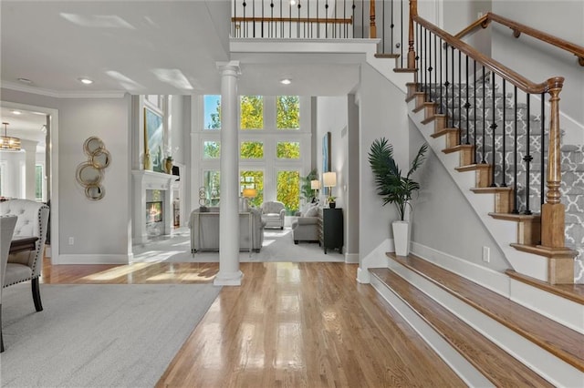 foyer entrance with ornamental molding, a high ceiling, decorative columns, and light hardwood / wood-style floors