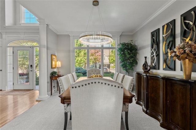 dining space with light wood-type flooring, a chandelier, ornamental molding, and decorative columns