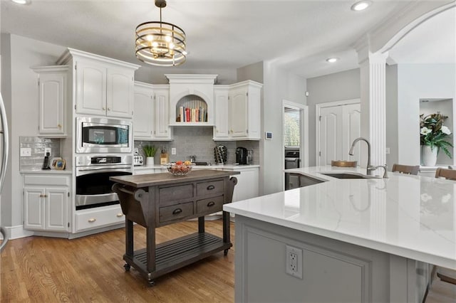 kitchen featuring sink, white cabinetry, light wood-type flooring, appliances with stainless steel finishes, and decorative light fixtures