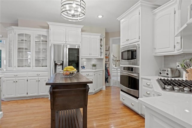 kitchen featuring white cabinets, appliances with stainless steel finishes, backsplash, and light hardwood / wood-style flooring