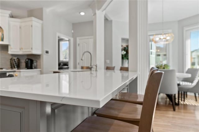 kitchen featuring ornate columns, white cabinets, hanging light fixtures, light hardwood / wood-style floors, and a breakfast bar area