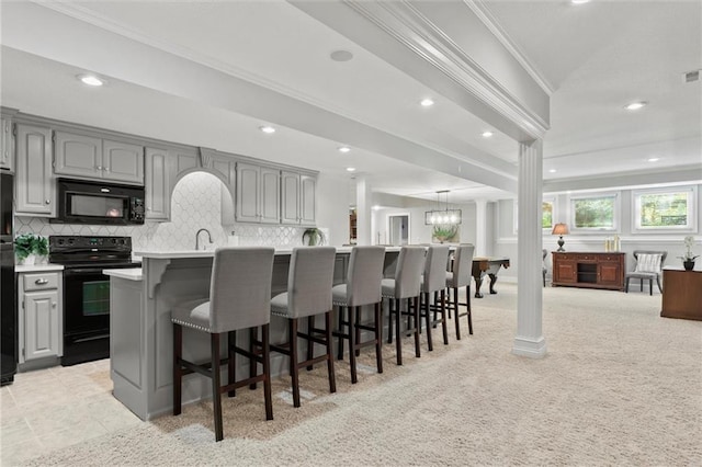 kitchen featuring a kitchen island with sink, black appliances, a breakfast bar area, and gray cabinetry