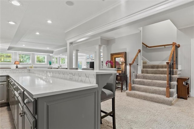 kitchen with light carpet, decorative columns, gray cabinetry, ornamental molding, and a kitchen breakfast bar