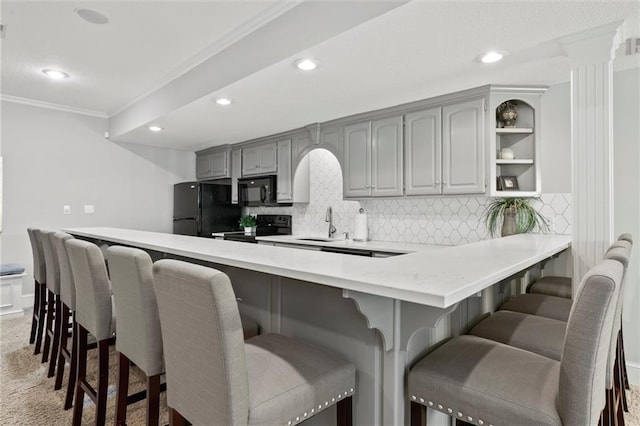 kitchen with black appliances, gray cabinetry, tasteful backsplash, and a breakfast bar