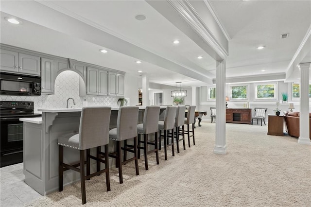 kitchen featuring ornate columns, black appliances, gray cabinets, a kitchen breakfast bar, and a kitchen island