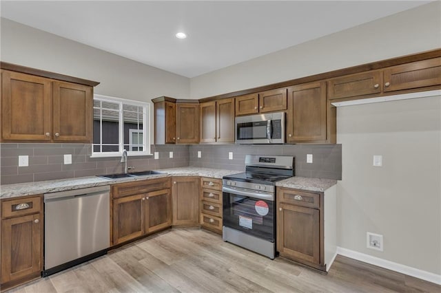 kitchen featuring sink, light stone counters, light hardwood / wood-style flooring, decorative backsplash, and appliances with stainless steel finishes