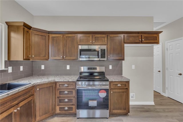 kitchen with sink, tasteful backsplash, light stone counters, light hardwood / wood-style floors, and appliances with stainless steel finishes