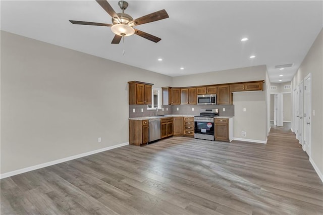 kitchen featuring ceiling fan, sink, stainless steel appliances, backsplash, and light wood-type flooring