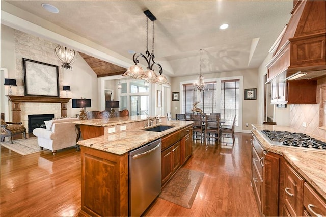 kitchen featuring dark wood-type flooring, decorative light fixtures, a fireplace, a center island with sink, and appliances with stainless steel finishes