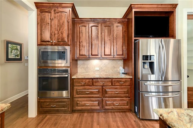 kitchen featuring hardwood / wood-style flooring, backsplash, light stone counters, and stainless steel appliances