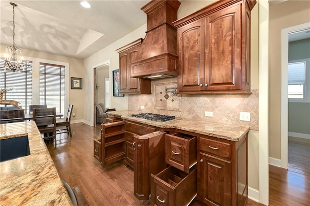 kitchen with light stone countertops, hanging light fixtures, stainless steel gas cooktop, dark hardwood / wood-style flooring, and custom exhaust hood