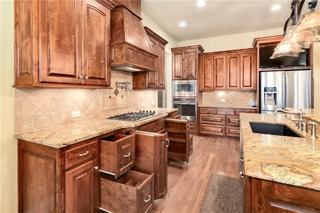 kitchen featuring premium range hood, light stone counters, stainless steel appliances, sink, and light hardwood / wood-style floors