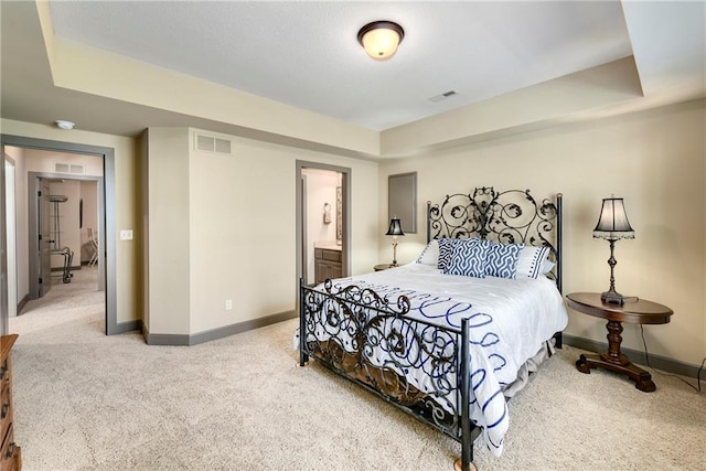 bedroom with carpet, ensuite bathroom, and a raised ceiling