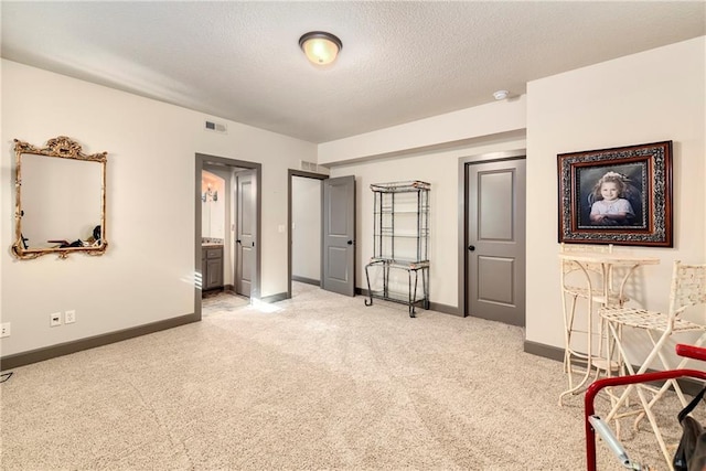 bedroom with connected bathroom, light colored carpet, and a textured ceiling