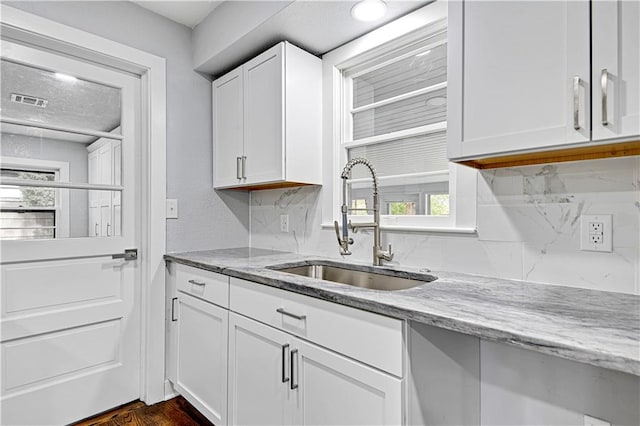 kitchen with light stone countertops, tasteful backsplash, sink, dark hardwood / wood-style floors, and white cabinetry