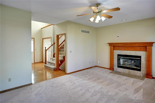 unfurnished living room with a tile fireplace, light colored carpet, and ceiling fan