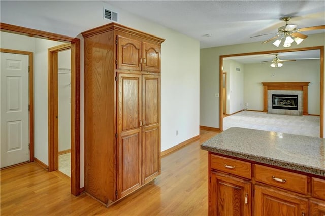 kitchen featuring ceiling fan, light hardwood / wood-style floors, light stone countertops, and a tile fireplace