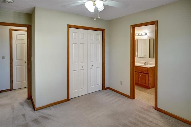 unfurnished bedroom with a closet, ensuite bath, ceiling fan, and light colored carpet