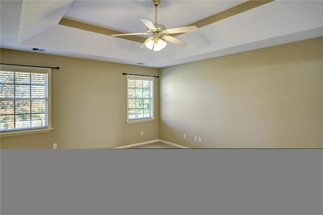 spare room with a raised ceiling, a wealth of natural light, and ceiling fan