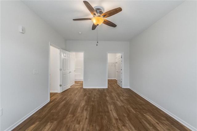 unfurnished bedroom featuring a closet, a spacious closet, ceiling fan, and dark hardwood / wood-style floors