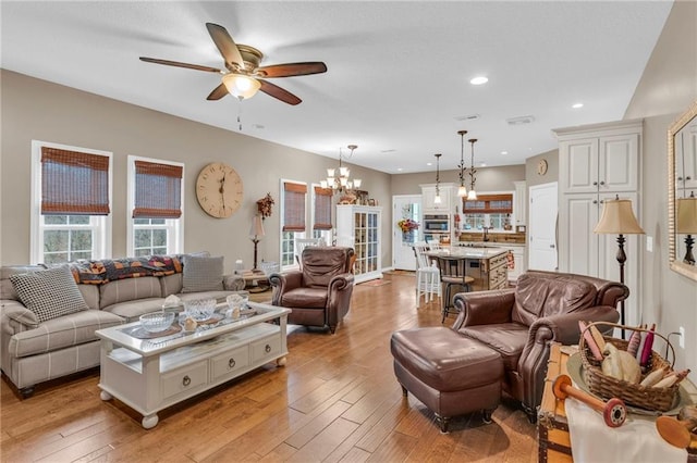 living room with light hardwood / wood-style floors and ceiling fan with notable chandelier