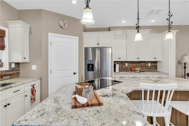 kitchen with light stone counters, pendant lighting, stainless steel refrigerator with ice dispenser, and backsplash