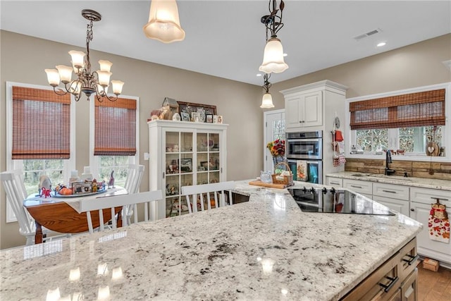 kitchen featuring black electric stovetop, white cabinets, a notable chandelier, sink, and decorative light fixtures