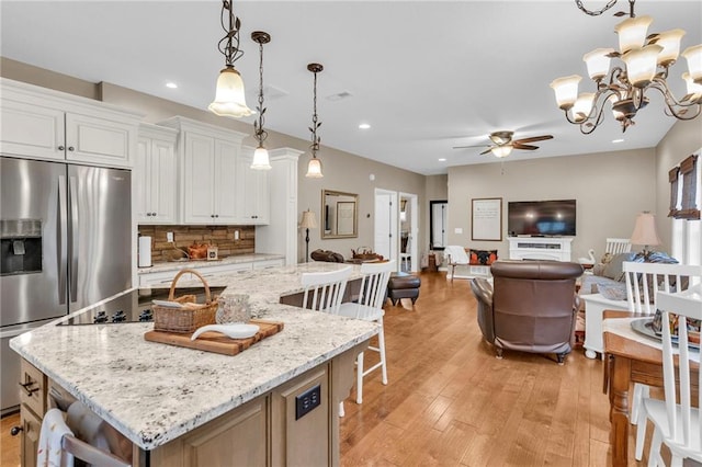 kitchen featuring light stone counters, light wood-type flooring, a spacious island, white cabinets, and pendant lighting