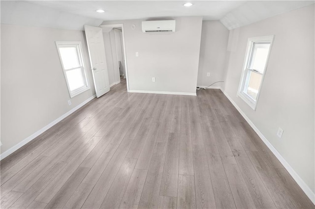 spare room featuring a wall mounted AC, light wood-type flooring, and vaulted ceiling