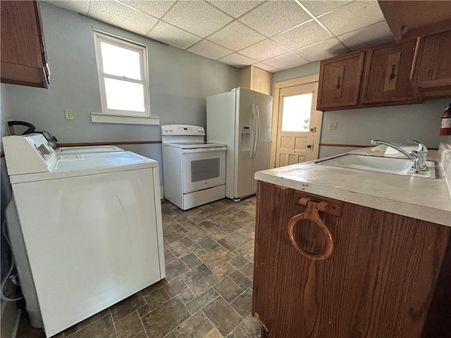 kitchen with white appliances, plenty of natural light, sink, washing machine and dryer, and a drop ceiling