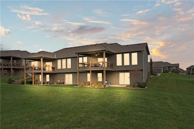 back house at dusk with a balcony and a yard