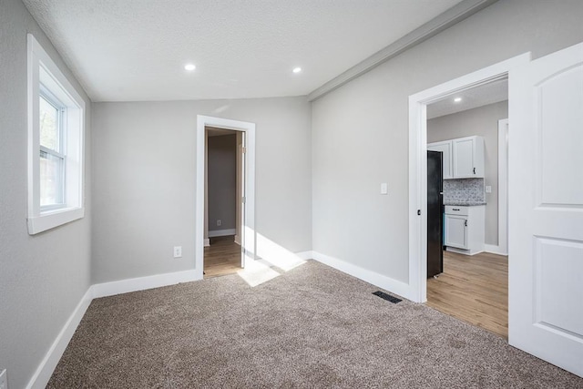 empty room featuring light colored carpet, a textured ceiling, and vaulted ceiling